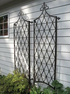 an iron trellis on the side of a house with potted plants next to it