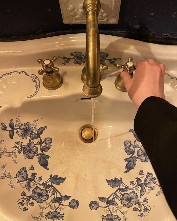 a person washing their hands in a sink with blue and white designs on the water