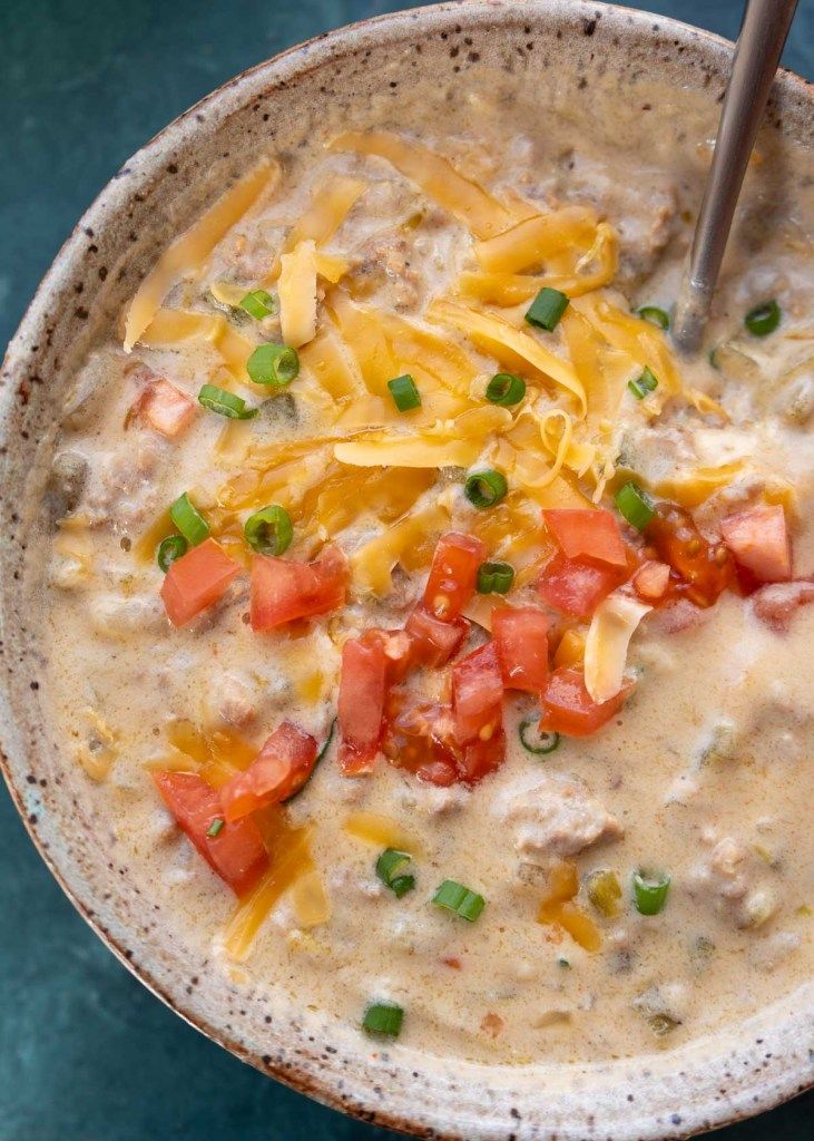 a bowl of soup with cheese, tomatoes and green onions in it on a blue surface