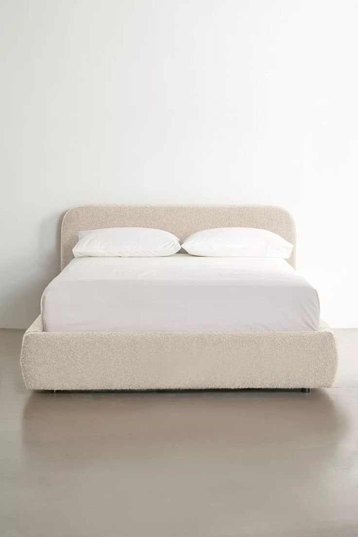 a white bed with two pillows on top of it next to a wall and floor