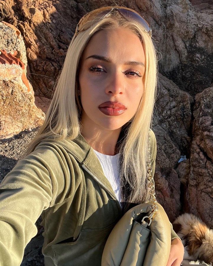 a woman taking a selfie with her dog in the mountains behind her on a sunny day