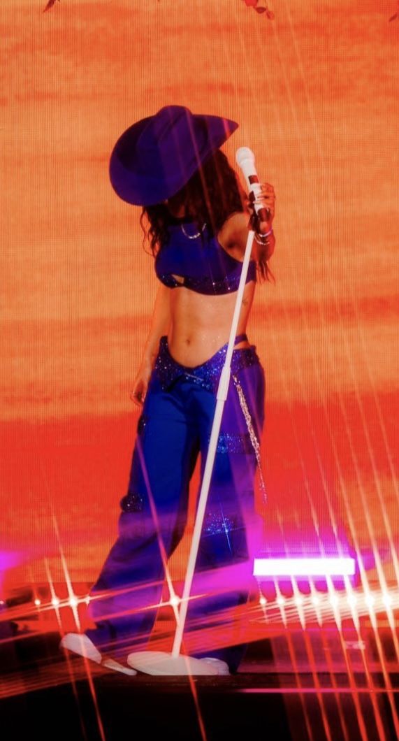 a woman in blue pants and a hat holding a white pole while standing under an umbrella