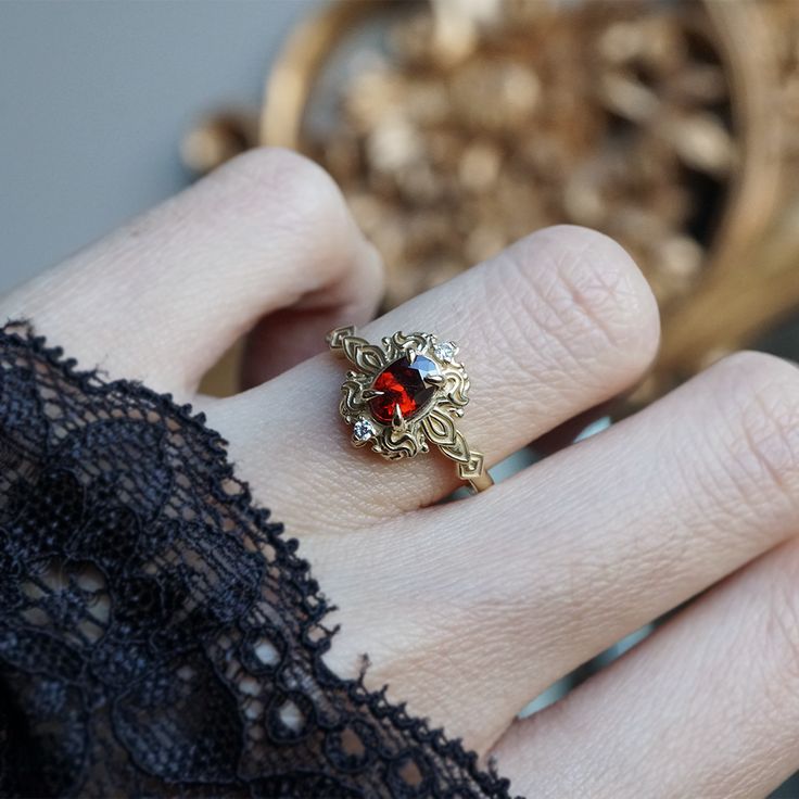 a close up of a person's hand wearing a ring with a red stone