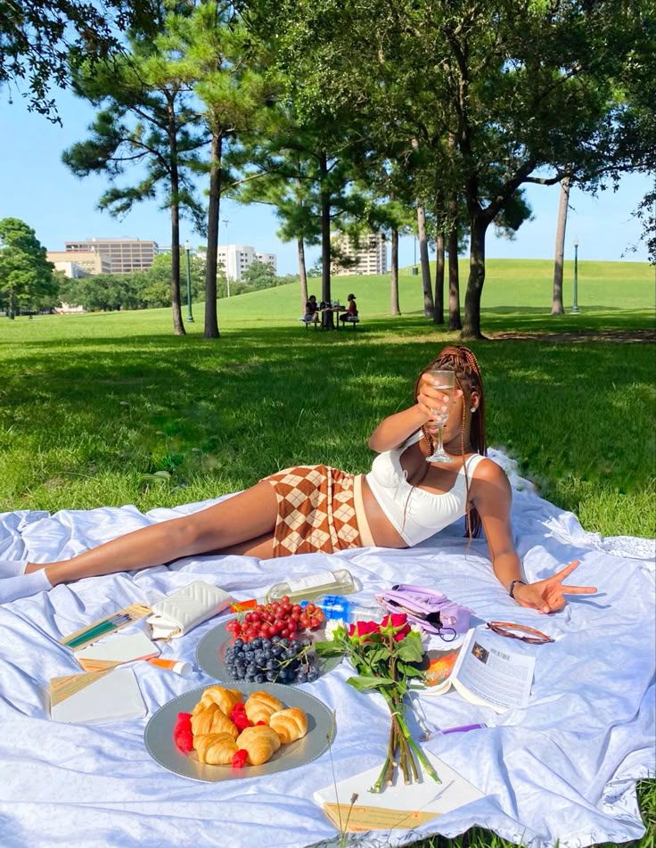 a woman laying on top of a white blanket next to a plate of fruit and vegetables