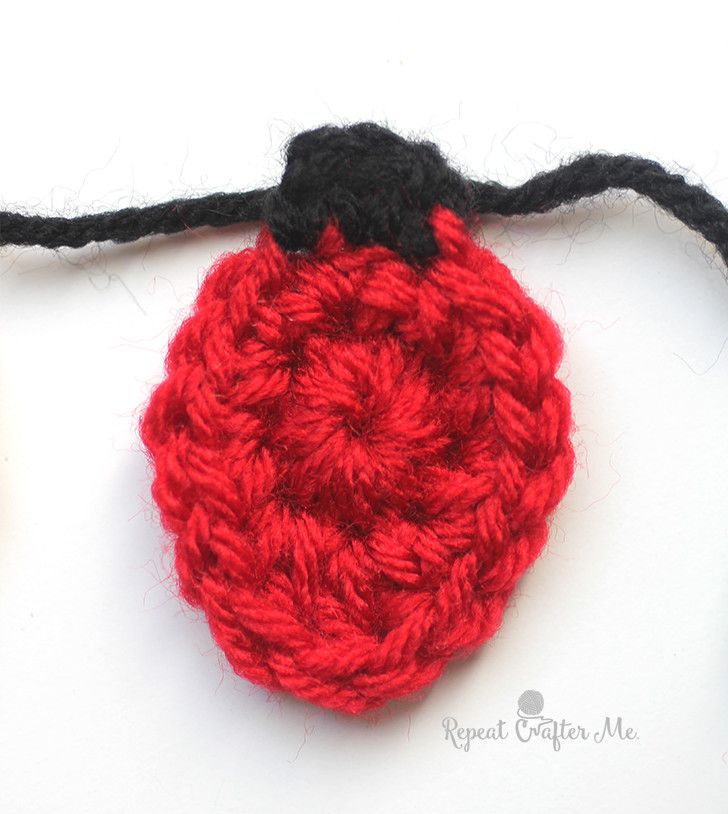 a crocheted red ornament on a white surface with black cord and two buttons