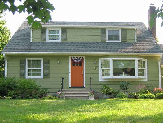 a green house with a red door and white trim on the windows, grass in front