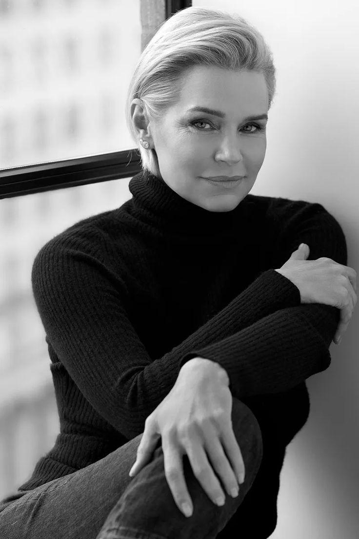 a black and white photo of a woman leaning against a wall with her arms crossed