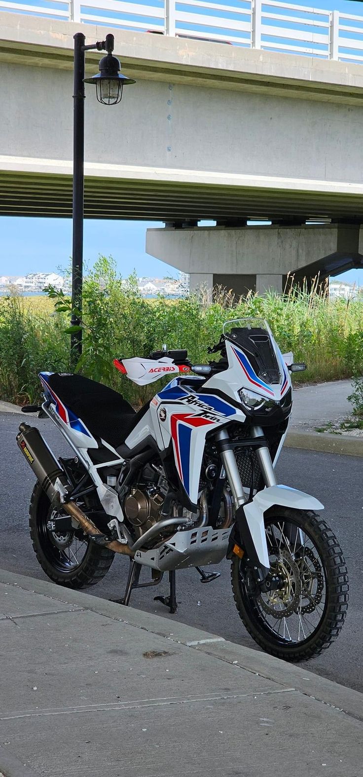 the motorcycle is parked on the side of the road by the street light and under an overpass