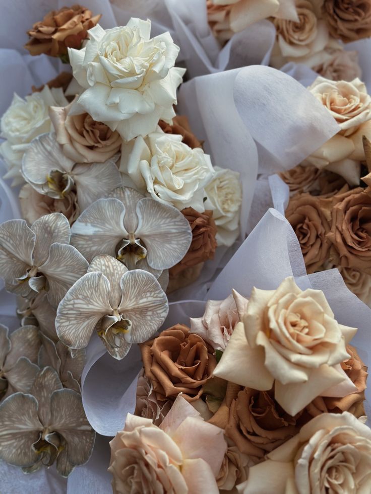 many different types of flowers are arranged on white tissue paper with brown and cream colors