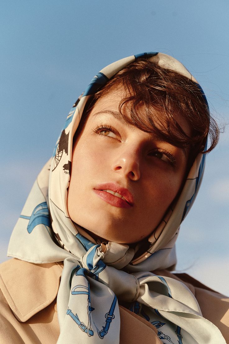 a woman with a scarf around her head looking off into the distance, against a blue sky