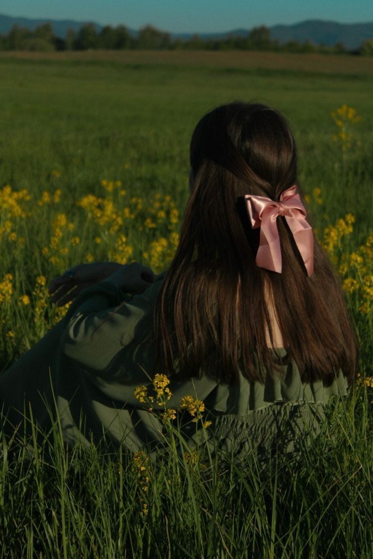 a woman sitting in the grass with a pink bow on her head and long hair