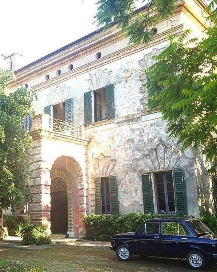 an old car is parked in front of a large stone building with green shutters