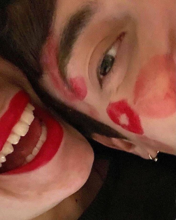 a man with his face painted like a clown has scissors in his mouth and is smiling at the camera