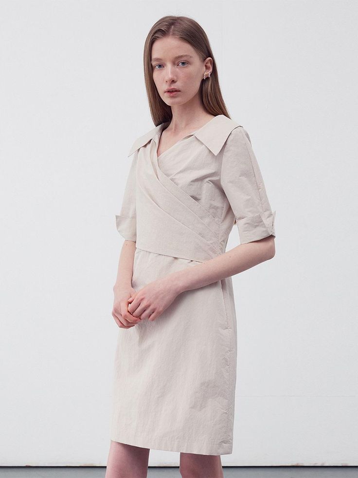 This product is a draped wrap shirt dress that elegantly combines tailored elements with a soft, feminine drape. The dress features a pronounced collar and a V-neckline, leading into a wrap front that ties at the waist, creating a figure-flattering silhouette. Its cuffed short sleeves add a structured detail to the otherwise fluid design. - The wrap style allows for an adjustable fit, catering to various body shapes.- Crafted from a light fabric, the dress is comfortable and suitable for day-long wear.- Its knee-length hem makes it versatile for both office environments and casual outings.- The draped design not only adds elegance but also ensures the dress moves beautifully with the wearer. Spring Wrap Dress With Draped Sleeves And Surplice Neckline, Spring Office Wrap Dress In Midi Length, Spring Office Wrap Dress Midi Length, Elegant Draped Midi Dress For Daywear, Drape Shirt Dress, Feminine Midi Dress With Surplice Neckline For Daywear, Chic Draped Wrap Dress For Formal Occasions, Elegant Collared Dress With Tie Waist, Chic Formal Draped Wrap Dress