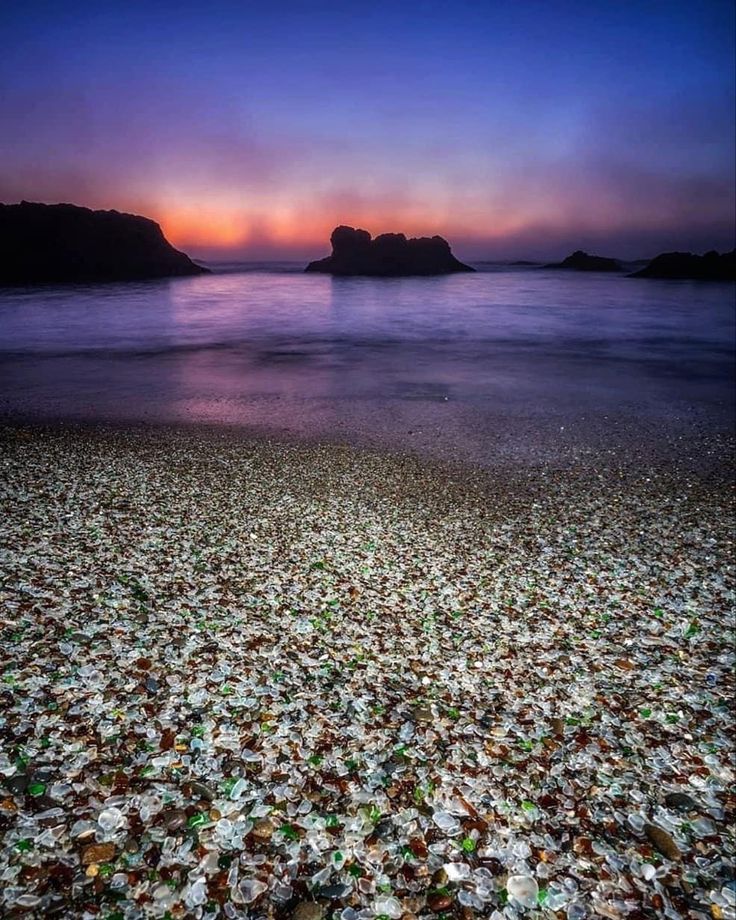 the beach is covered in sea glass at sunset or sunrise, with an island in the distance