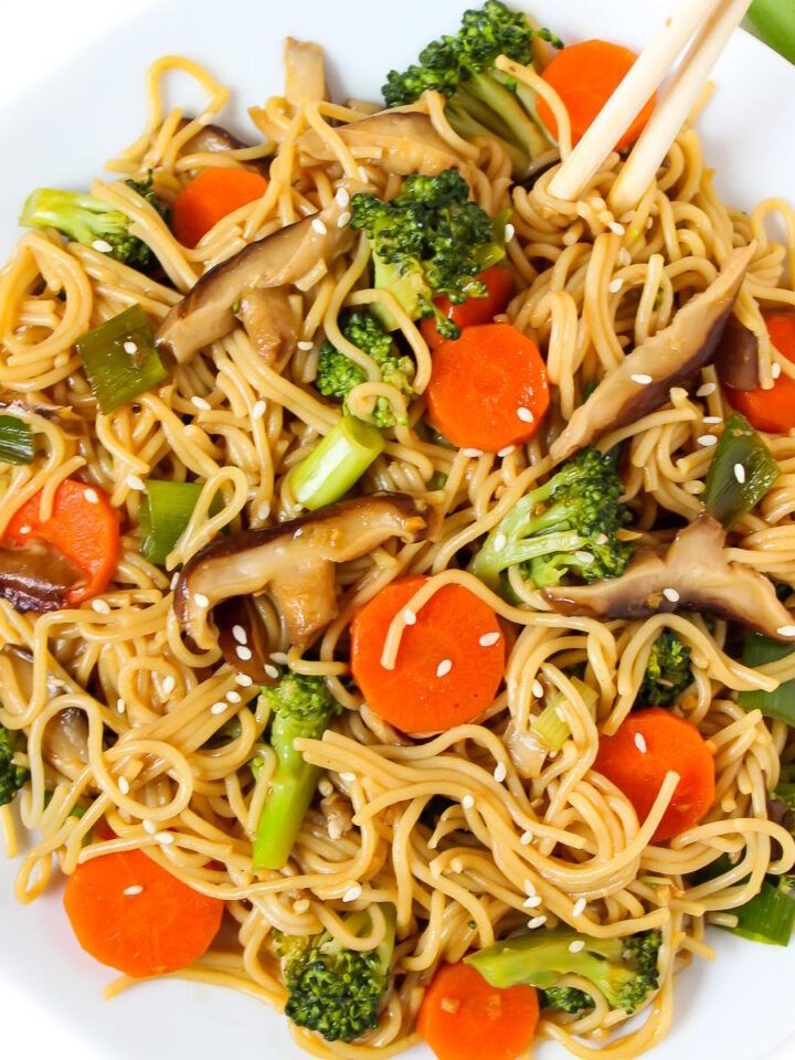 noodles with carrots, broccoli and mushrooms on a white plate topped with chopsticks