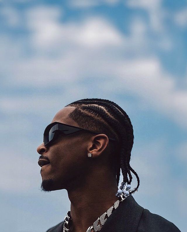 a man with dreadlocks wearing sunglasses and a black jacket looking off into the distance