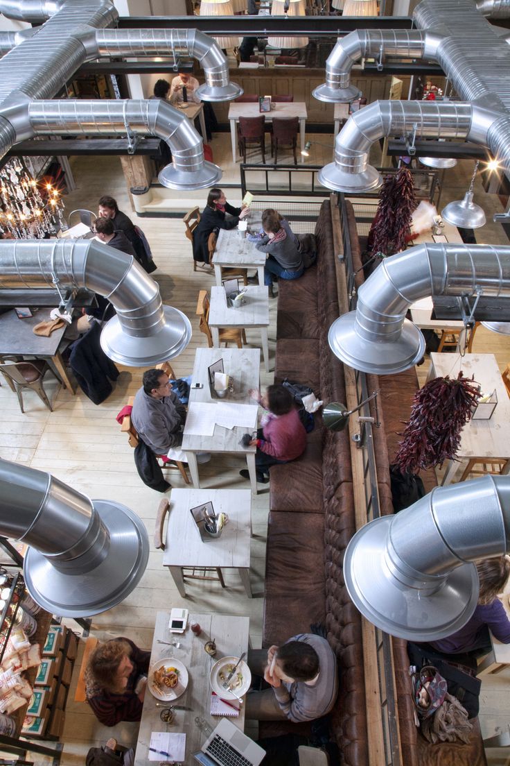 an overhead view of people sitting at tables in a restaurant with large metal pipes on the ceiling