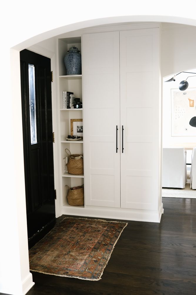 a white closet with black doors and shelves in the corner next to a brown rug