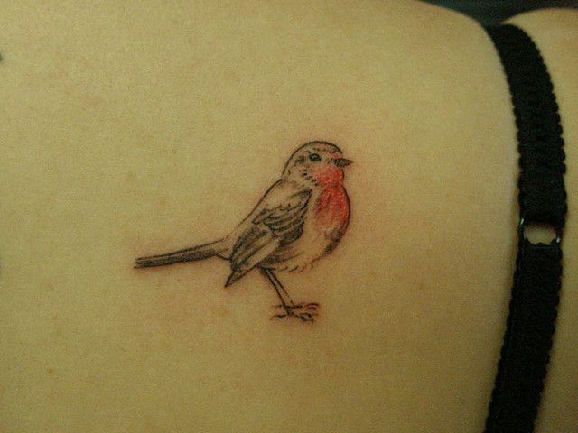 a small bird tattoo on the back of a woman's left upper arm and shoulder