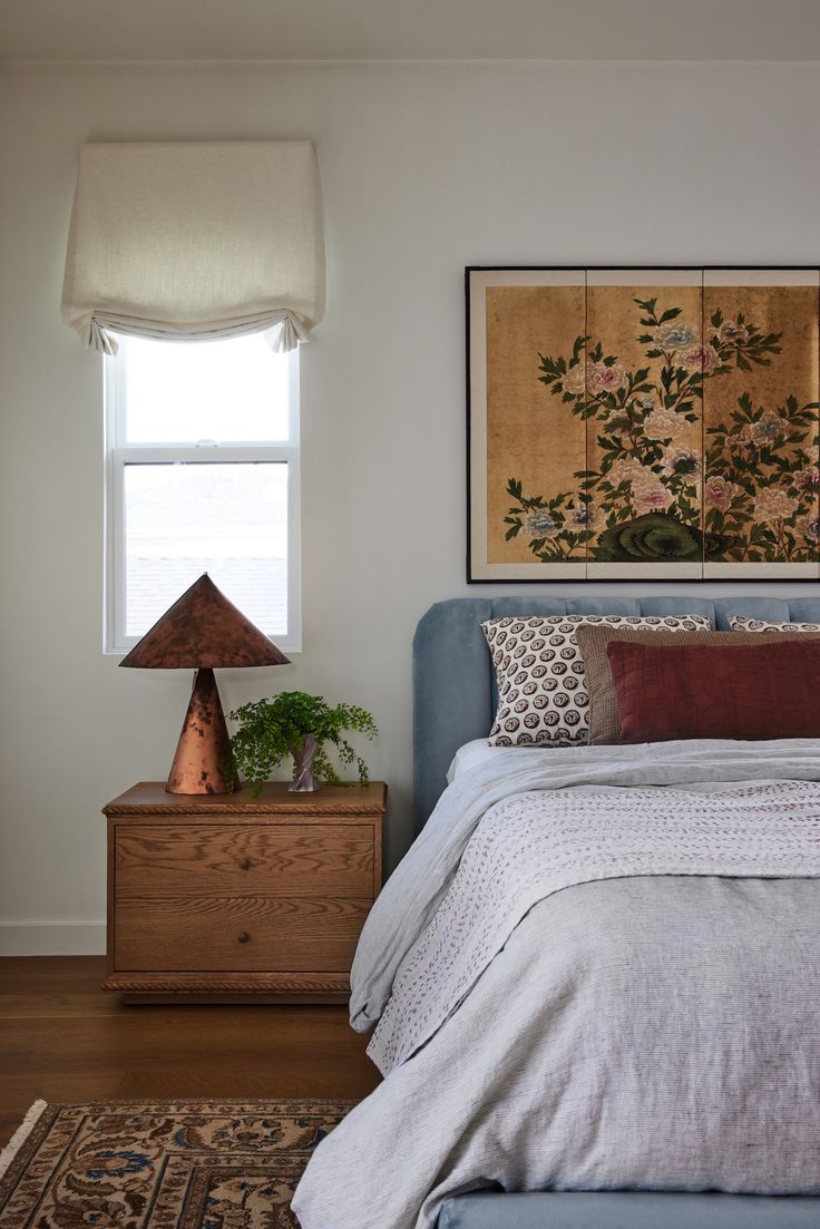 a bed sitting under a window next to a wooden dresser with a lamp on top of it