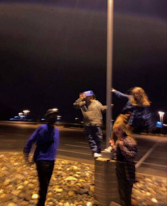 three people standing on the side of a road next to a street light at night