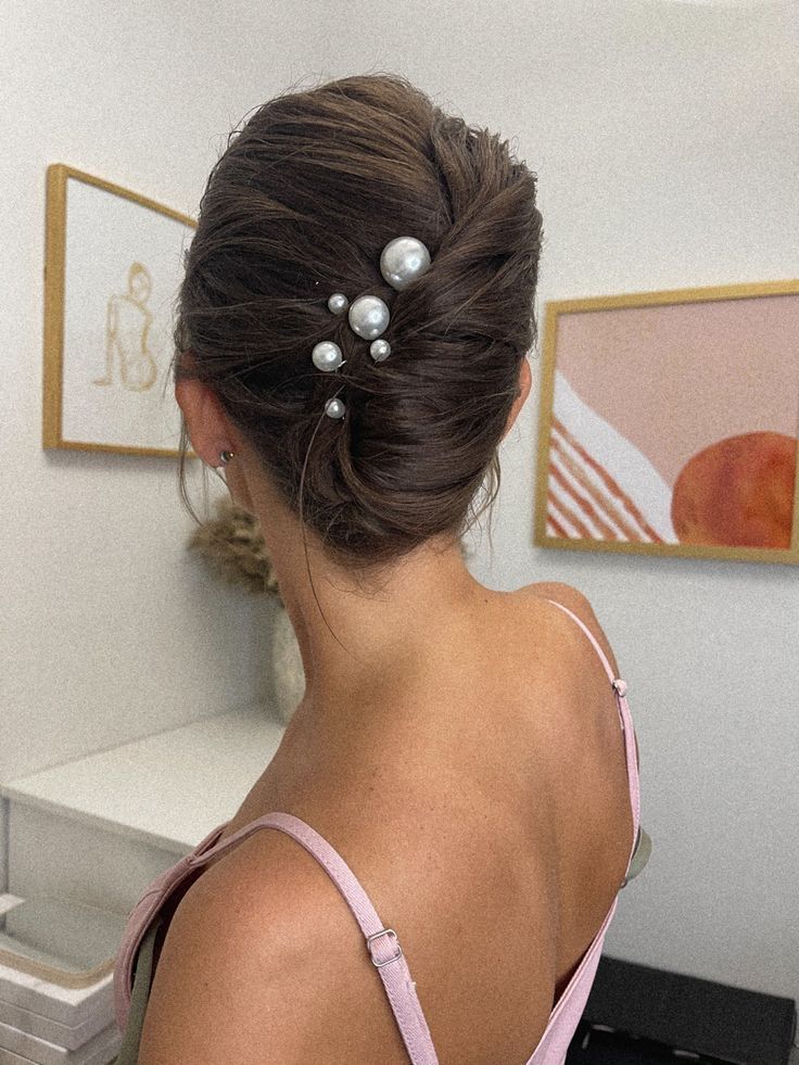 a woman with her hair in a low bun and pearls pinned to the side of her head