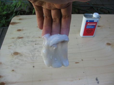 a person holding something in their left hand on top of a wooden table next to a bottle