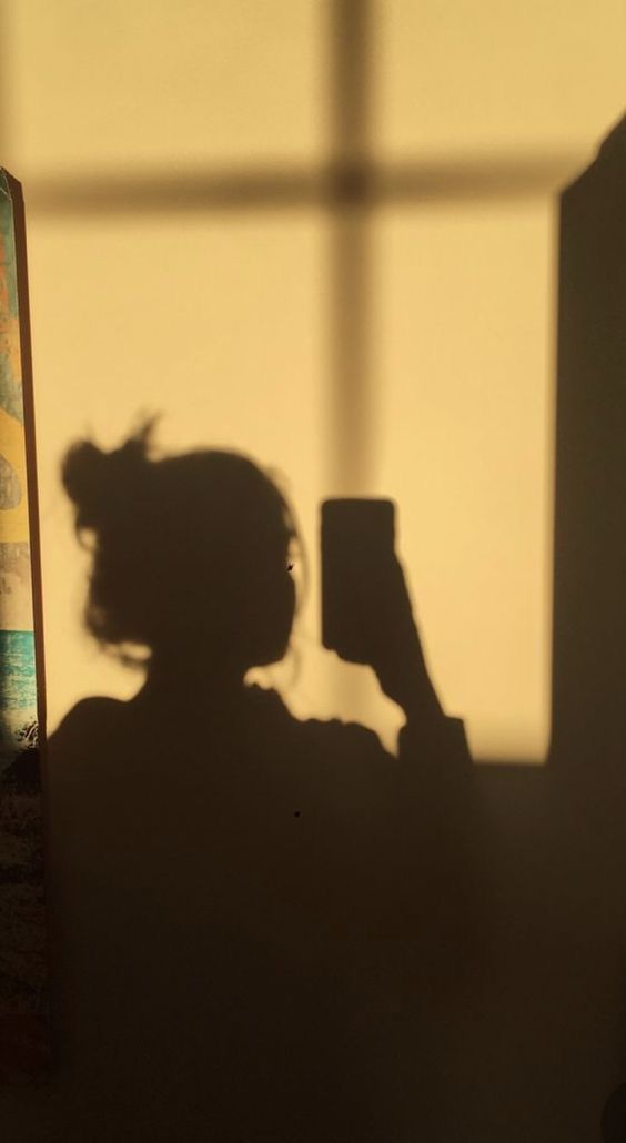 the shadow of a person holding a cell phone in front of a window with a painting behind it