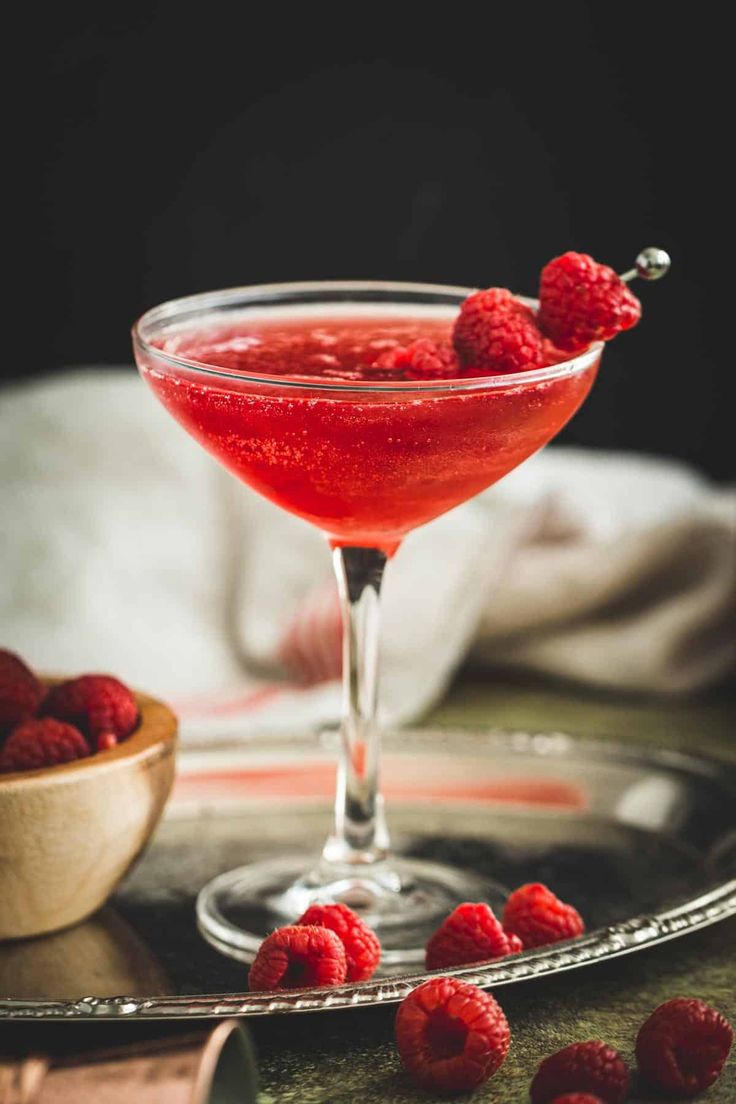 raspberry martini in a coupe glass with fresh raspberries on the rim