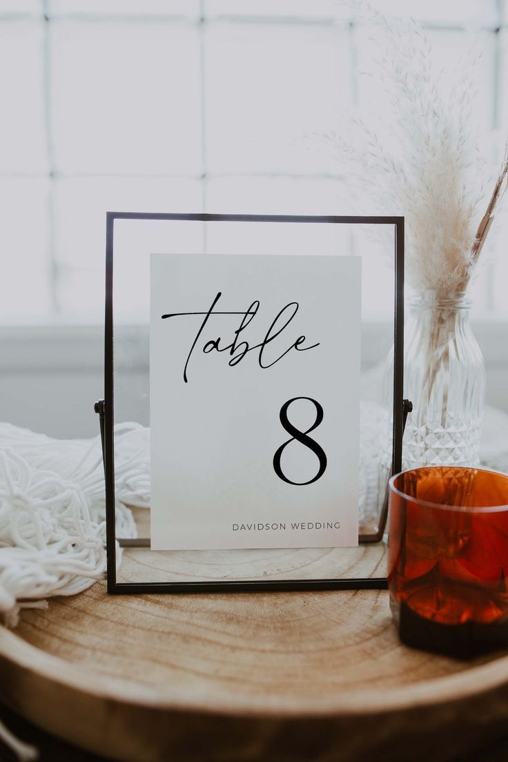 a wooden table topped with a sign next to a glass filled with liquid and a candle