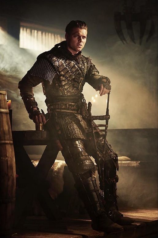 a man in armor is sitting on a chair and posing for the camera with his hands on his hips