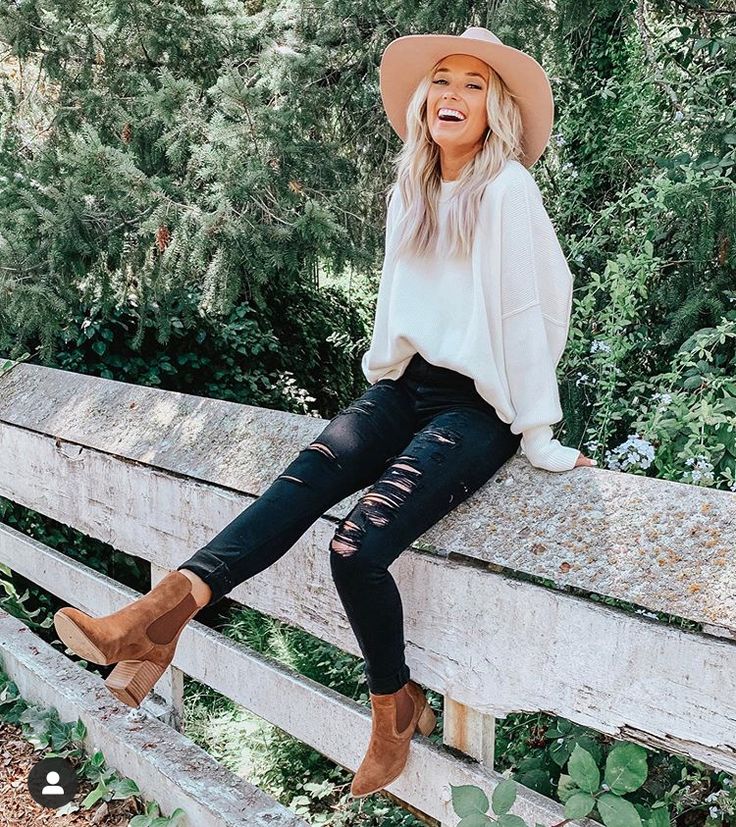 a woman sitting on top of a wooden fence wearing a hat and black ripped jeans