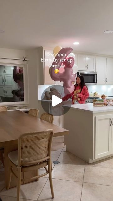 a woman standing in a kitchen next to a table with chairs and a microwave oven