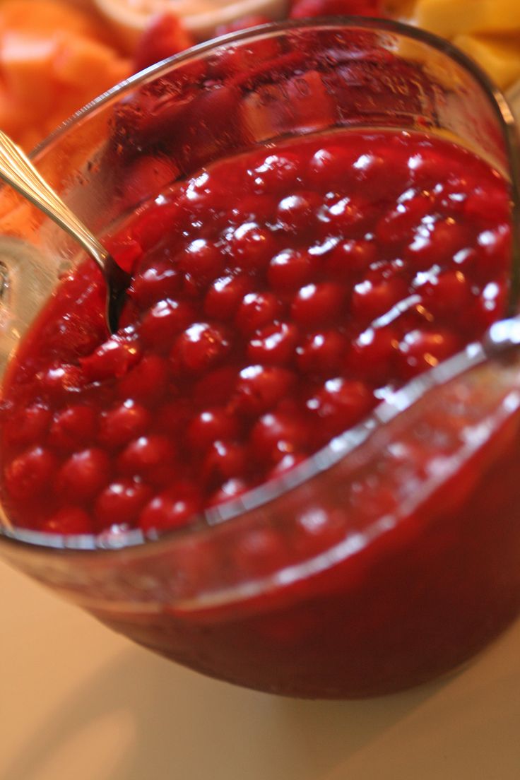 a glass bowl filled with cranberry sauce next to sliced oranges