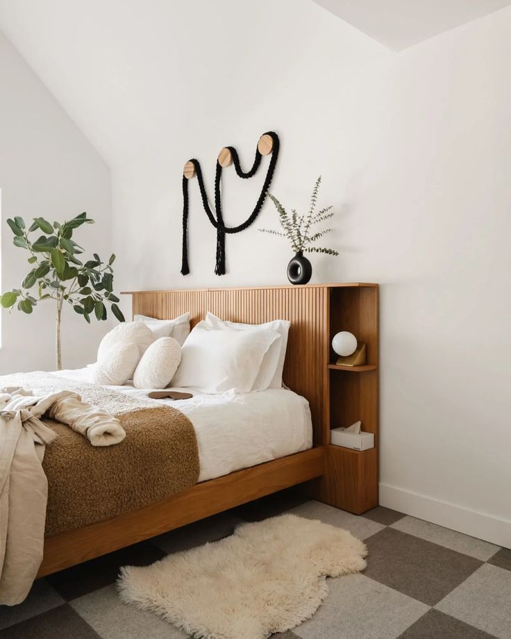 a bed with white sheets and pillows in a bedroom next to a potted plant