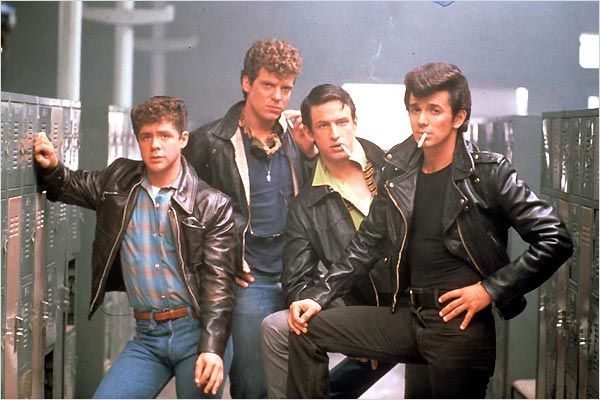 four young men in leather jackets leaning against lockers with their hands on the hips