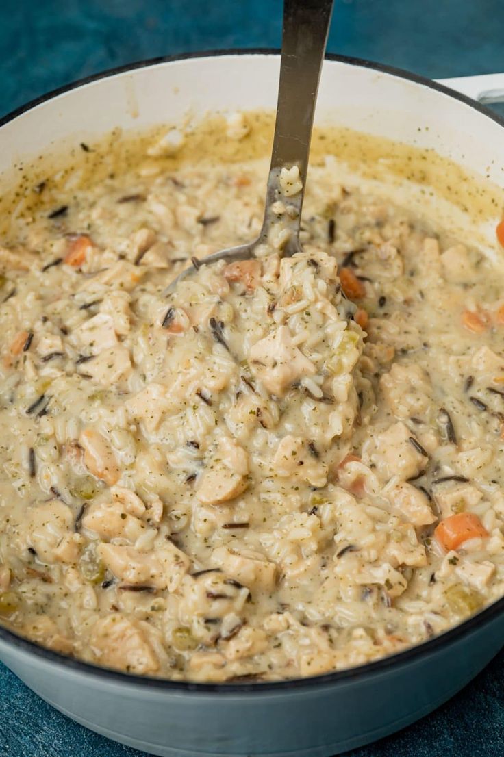 a pot filled with rice and carrots on top of a blue tablecloth next to a spoon