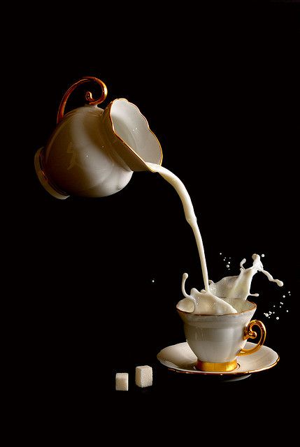 milk being poured into a teacup with sugar cubes on the saucer in front of it