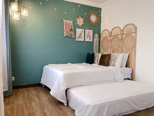 two beds in a room with blue walls and wood flooring that has lights strung from the ceiling