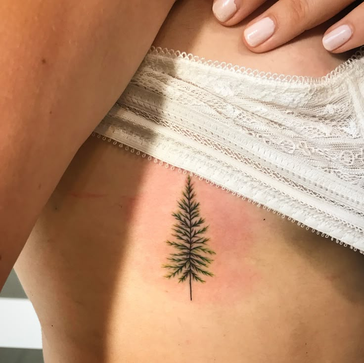 a woman's back with a small tattoo of a pine tree on her left side