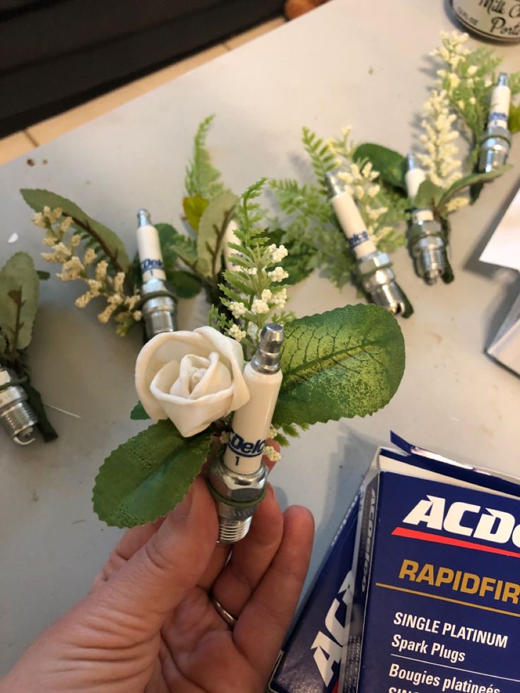 someone is holding a fake white rose with green leaves and some razors next to it