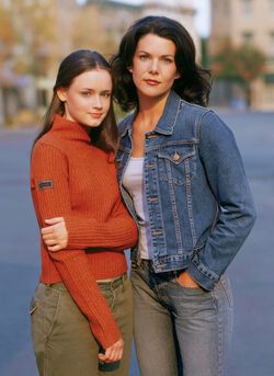 two young women standing next to each other on the side of a road with buildings in the background