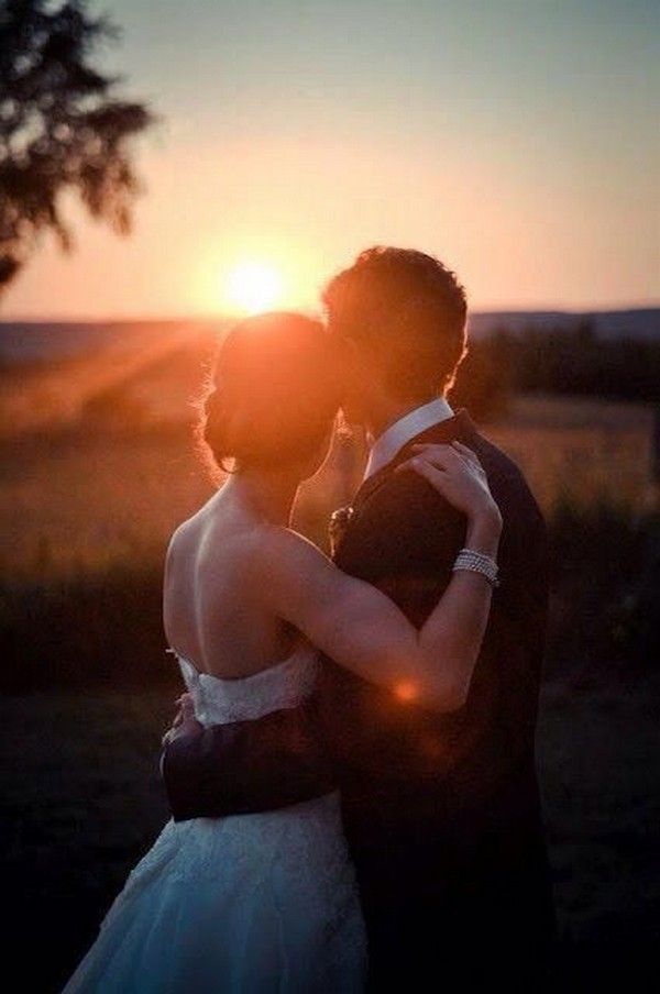 a bride and groom kissing in front of the sun