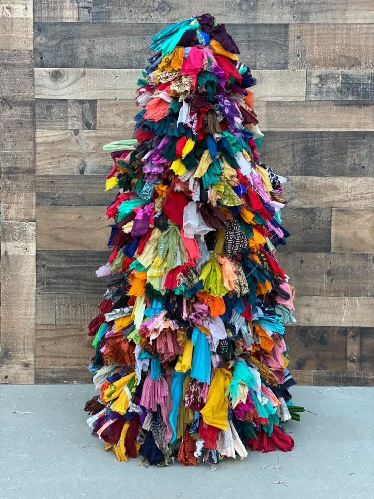 a multicolored christmas tree made out of old clothes on display in front of a wooden wall