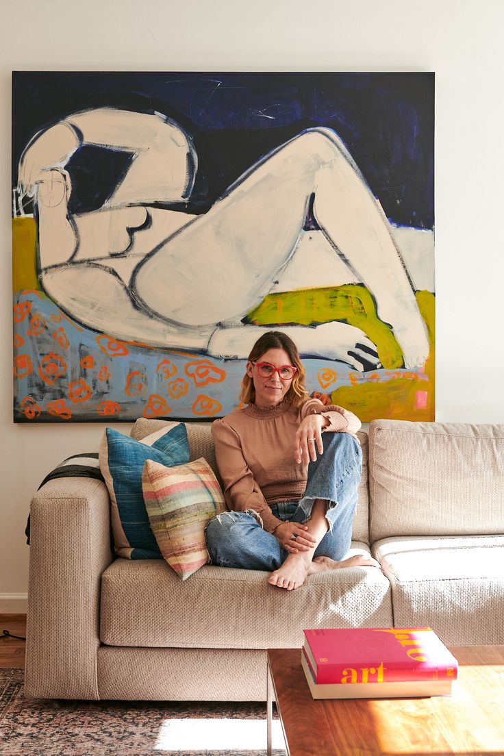 a woman sitting on top of a couch next to a painting