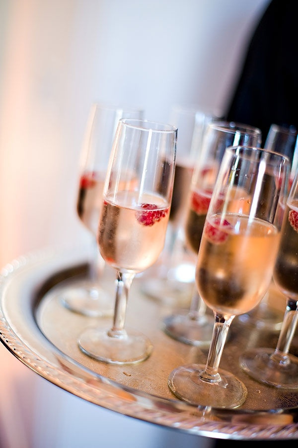 several glasses of champagne on a tray with strawberries in the bottom one glass is half full