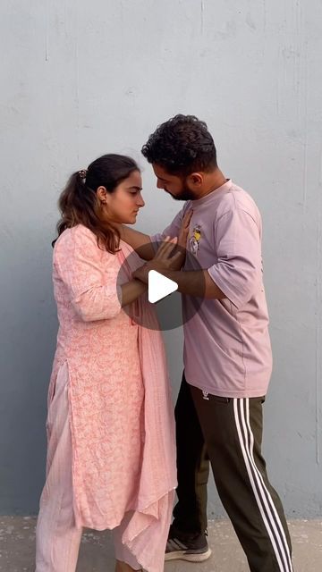 a man and woman standing next to each other near a wall with their hands together