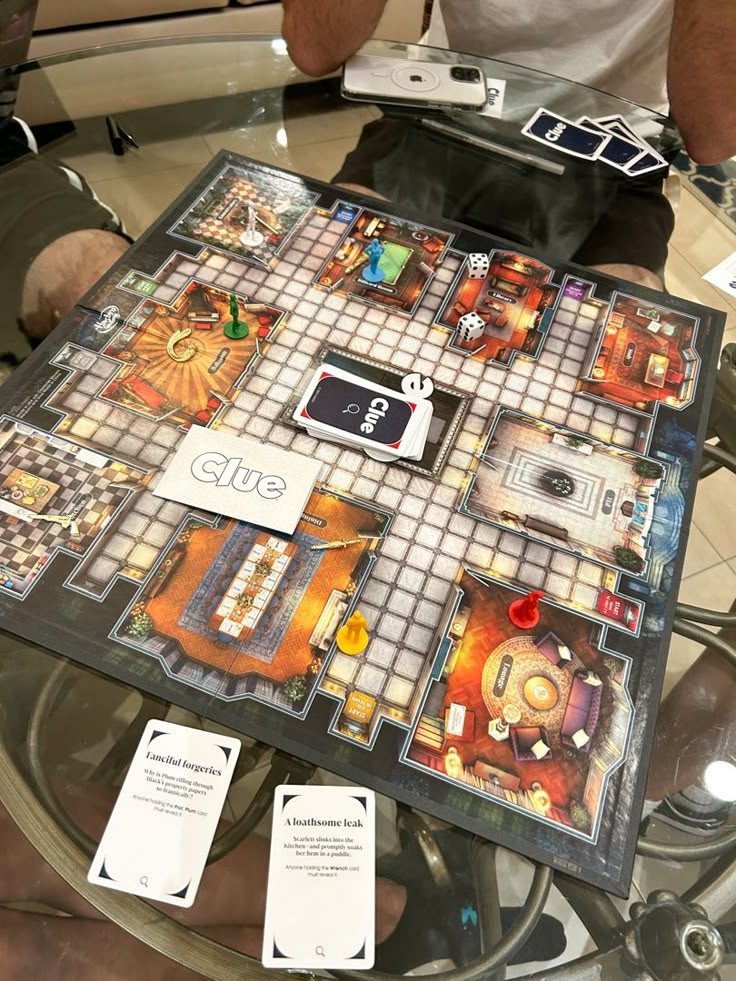 a board game sitting on top of a glass table next to a person holding a cell phone