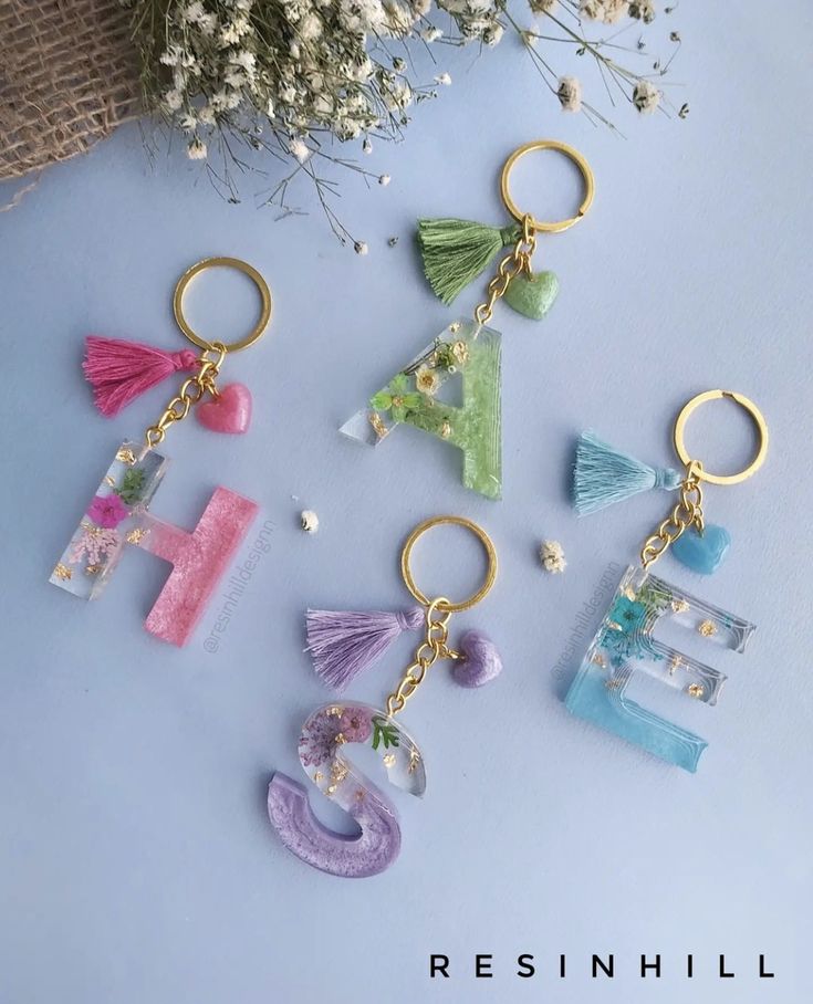 four different key chains with letters and tassels hanging from them on a blue surface